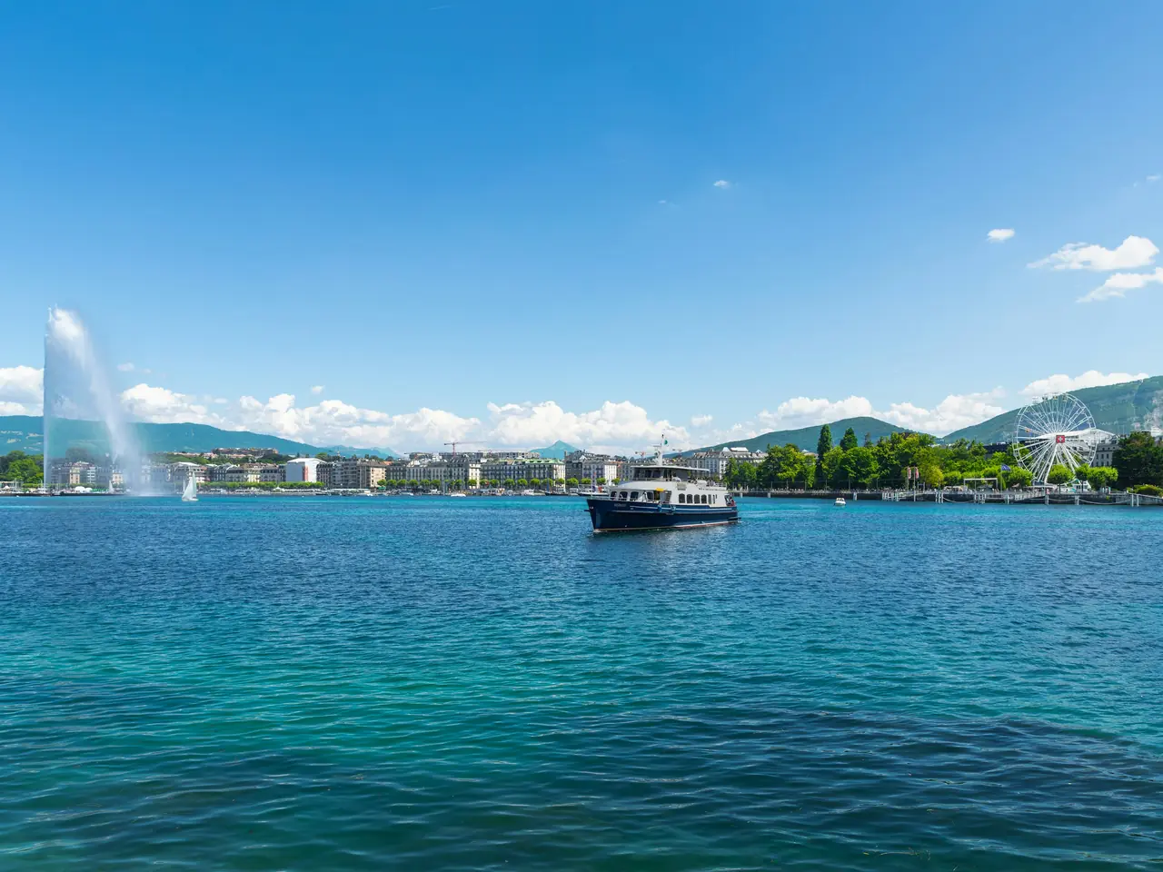 La rade de Genève par beau temps : le jet d’eau, un bateau et la grande roue sur le quai.