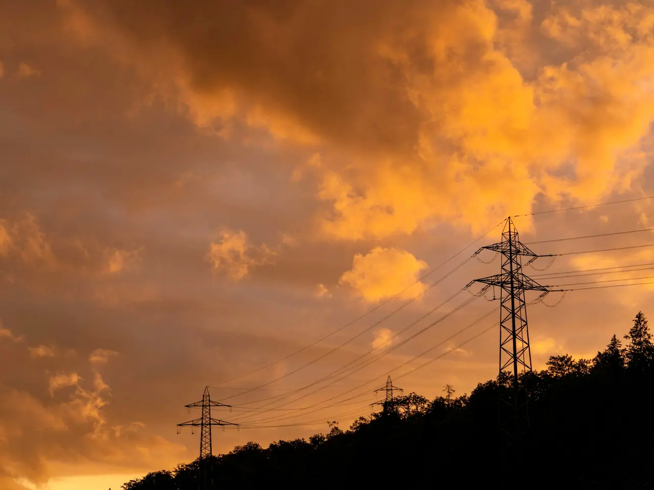 Une ligne à haute tension sur une crête boisée, sous un ciel orange de fin de journée.